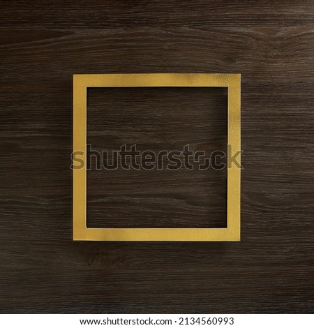 Golden square frame on a dark brown wooden background. Text space. Top view. Minimal style.