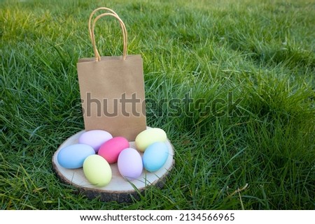 An Easter paper bag and multi-colored eggs on a wooden stand stand on the grass. Easter concept, holiday, customs ,family, religion 