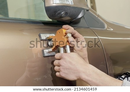 The hands of a professional painter repairing dents without painting. Royalty-Free Stock Photo #2134601459