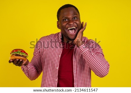 young african american man eating hamburger screaming isolated on yellow background.sale concept