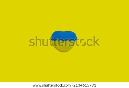 A stone in the shape of a heart is painted in the colors of the Ukrainian flag. A hole in yellow against a blue background from a military shell. 