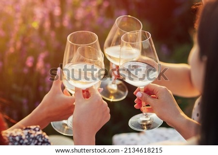 A group of girlfriends raise a toast with glasses of white colored wine on a sunset. Close shot. Royalty-Free Stock Photo #2134618215