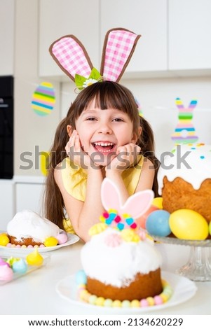 A cute smiling little girl with bunny ears prepares an Easter cake and painted eggs. Religious holiday. 