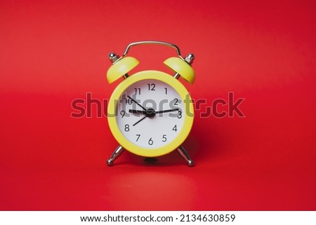 Bright yellow retro alarm clock isolated on red paper background with space for text. Time, minutes, hours concept. The value of time in business and life. Clock showing nine hours and 14 minutes. Royalty-Free Stock Photo #2134630859
