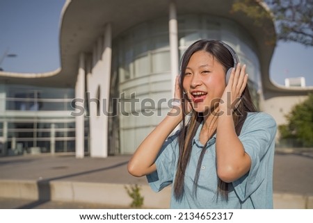 Young beautiful asian girl with headphones happy smiling and dancing in the street.