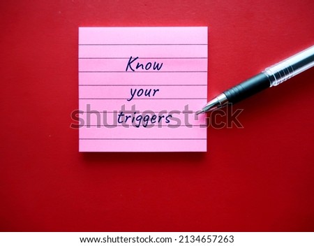On red background, pen writing on note pad KNOW YOUR TRIGGERS, learning to know experience of having emotional reaction to a disturbing topic in the media or social setting and empower to cope with it Royalty-Free Stock Photo #2134657263
