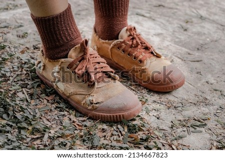 Torn student shoes, Poverty of rural schoolchildren often cannot afford new shoes, high school student legs wearing torn shoes, poor shortage of educational equipment, worn-out brown old sneakers Royalty-Free Stock Photo #2134667823