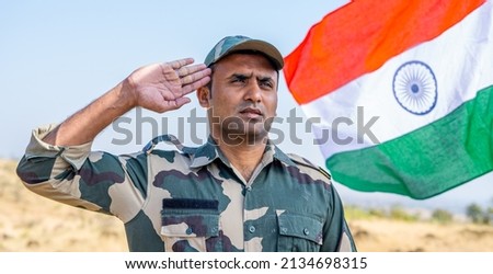 front view low angle shot of Proud Indian army soldier saluting while waving indian flag in background - concept of patriotic, nationalism, independence day celebration and honour