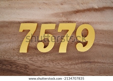 Wooden  numerals 7579 painted in gold on a dark brown and white patterned plank background.