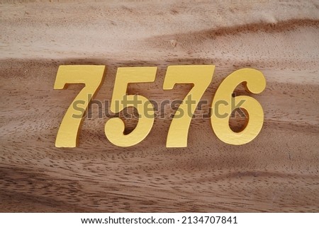 Wooden  numerals 7576 painted in gold on a dark brown and white patterned plank background.