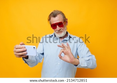 elderly man in fashionable red glasses with a phone yellow background