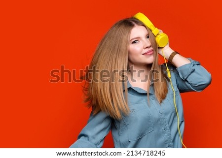 Funny young woman dance to favorite song moves to rhythm of music holds yellow headphone wears basic shirt expresses happiness. Hipster girl looking at camera and joy indoor. People lifestyle concept.