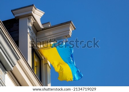 The national flag of Ukraine which has equally sized horizontal bands of blue and yellow, Ukraine flag hanging on rooftop of house in Amsterdam, Netherlands, Support Ukrainian from Russian attack war.