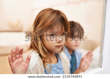 Trapped in a glass box of emotion. Shot of two unhappy-looking young children looking out a window on a rainy day. Royalty-Free Stock Photo #2134744891