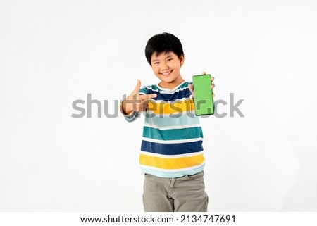 Young Asian Kid holding a phone in his hands with a green screen standing on a white isolated background with copy space.