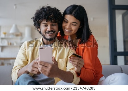 Smiling multiracial couple holding credit card shopping online, ordering food looking at digital screen sitting at cozy home. Happy freelancers receive payment, successful business Royalty-Free Stock Photo #2134748283