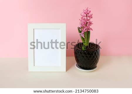 photo frame with white blank card and flowers on pastel pink background. Mock up poster frame. Stylish template.