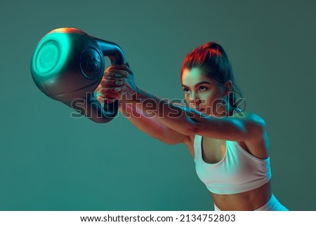 Portrait of sportive woman workout, doing exercises with sports equipment isolated on green studio background in neon light. Sport, gym, action, motion, beauty concept. Fitness, hobby, health Royalty-Free Stock Photo #2134752803