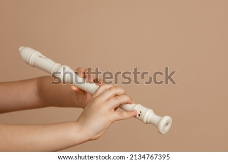 Hold fipple flute with both hands and pinch holes closeup, beige background. Woodwind musical instrument. Aerophone or reedless wind instrument that produce sound from flow of air across opening. Royalty-Free Stock Photo #2134767395