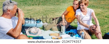 Senior father taking a photo with a camera to his happy family sitting on a blanket having picnic outdoors