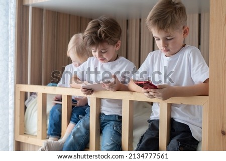 kids boys brothers play games on the phone, a new app for children's development. They are sitting on the second floor of a wooden bed,natural materials. Read a lot , audiobook or cartoons