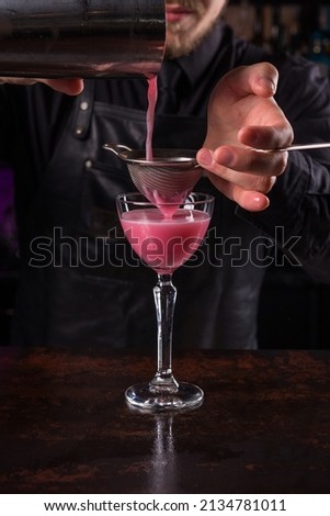 Bartender dressed in black apron and shirt make pink cocktail drink on black background