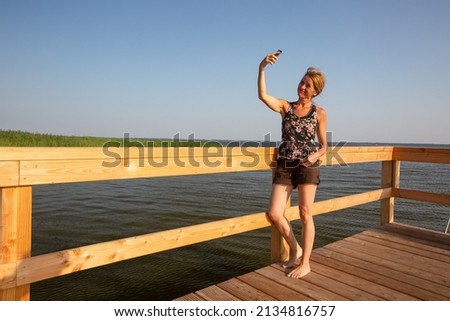 View of a relaxing mature woman standing on a pier taking a selfie - Mecklenburg Vorpommern, Germany - copy space
