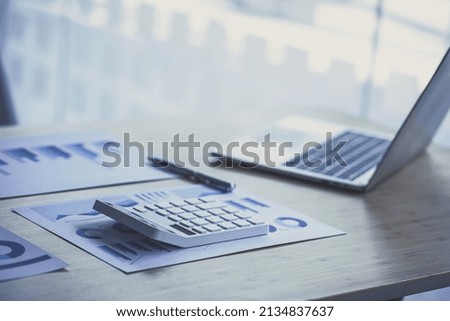 Office desk with supplies calculator laptop paper charts.
