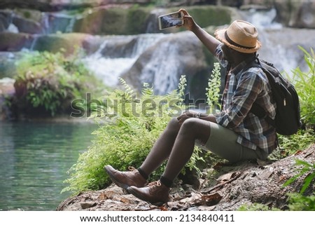 African Man Traveller with backpack sitting for selfie and relaxing freedom at the waterfall