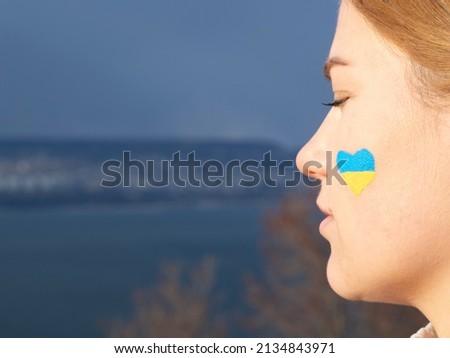 Side view portrait of girl with yellow-blue ukrainian flag in the shape of heart on her cheek