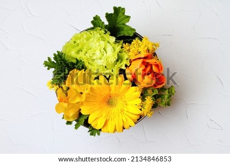 A colorful and delicate flower arrangement in a round box on the white wall background with copy space.