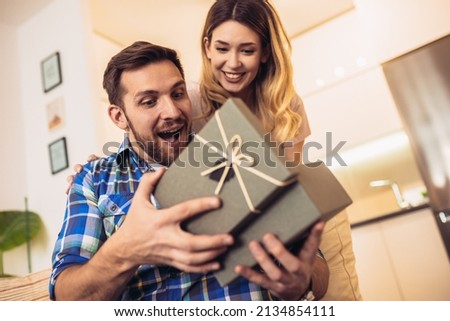 Romantic couple at home. Woman giving a present to her boyfriend.