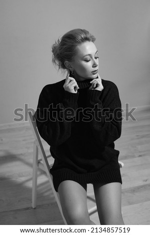 portrait of a fashionable young woman in a black cozy sweater sitting on a chair in the studio in autumn