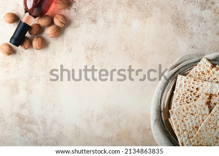 Passover celebration concept. Matzah, red kosher and walnut. Traditional ritual Jewish bread on sand color old concrete background. Passover food. Pesach Jewish holiday. Royalty-Free Stock Photo #2134863835