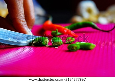 Stock photo of a girl cutting or chopping fresh organic green chili on dark pink color chopping board in the kitchen area at Bangalore, Karnataka, India.Picture captured under natural light.