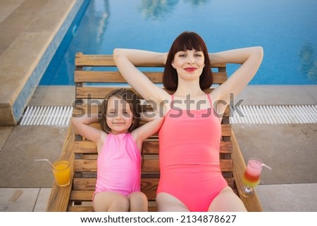 Top view of charming caucasian woman with cute little daughter joyful lying with pleasure with their hands behind their heads on deck chair. Spending time with family in nature concept. Copy space.