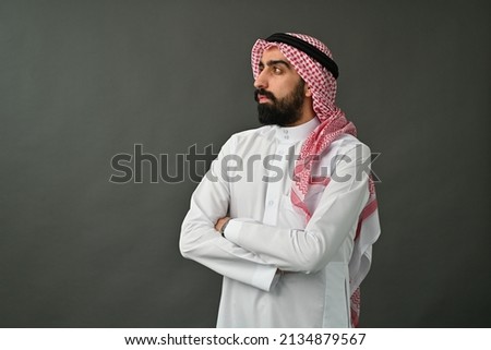 Saudi Arab man looking at side maybe towards a special offer thinking or choosing wearing traditional Arabian dress isolated on studio background Royalty-Free Stock Photo #2134879567