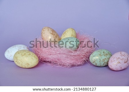 Yellow and green, red Easter eggs lie in pink nest and nearby. Lilac background. Copy space