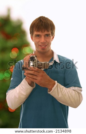 happy guy holding a camcorder; blurred christmas tree background