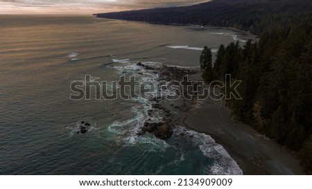 Sunset over the coast of the Pacific Ocean. pink skies over the emerald-green waters of Vancouver Island, CA where foamy waves meat the rocky coastline.