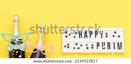 Purim background. Happy Purim written in lightbox, party props, masks, and champagne on a bright yellow background. Top view, copy space. Banner