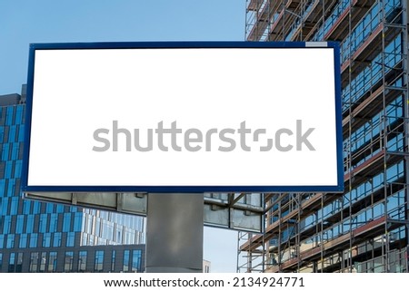 Advertising billboard mock-up next to modern office building with glass facade under construction