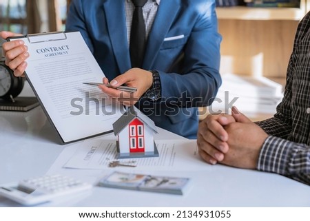 Discussion With A Real Estate Agent, a businesswoman signing a contract for Insurance protecting house, a real estate home is pointing to insurance contract signing and are explaining to customers.