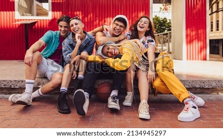 Youngsters having fun together in the city. Group of multiethnic young people laughing cheerfully while sitting together outdoors. Vibrant generation z friends making happy memories. Royalty-Free Stock Photo #2134945297