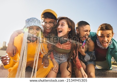 Youngsters having a good time together during the covid-19 pandemic. Group of happy friends laughing cheerfully while sitting on a wall. Multiethnic young people having fun and making memories. Royalty-Free Stock Photo #2134945305