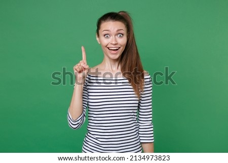 Excited shocked young brunette woman 20s wearing striped casual clothes posing holding index finger up with great new idea looking camera isolated on green color wall background, studio portrait Royalty-Free Stock Photo #2134973823