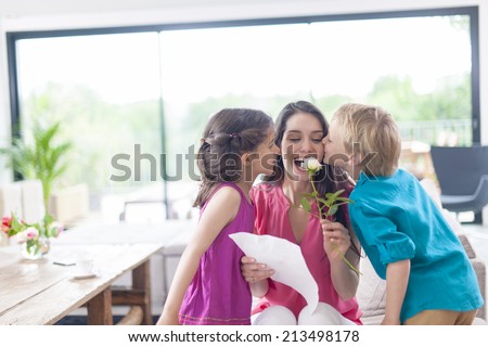 kids kissing their mother and offering a flower