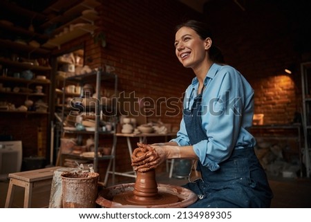 Happy smiling pretty female ceramicist wearing apron working with fresh wet clay in art studio
