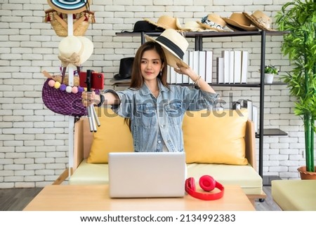 Fashion Asian blogger woman in jeans dress showing casual hats on camera. Stylist influencer girl showing trendy clothes filming vlog episode for her channel. Opinion leader set trends.