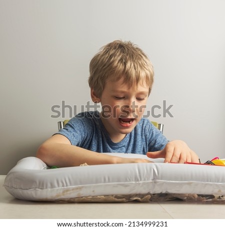 a boy with blond hair enthusiastically plays with sand in an inflatable sandbox for the house horizontal composition.